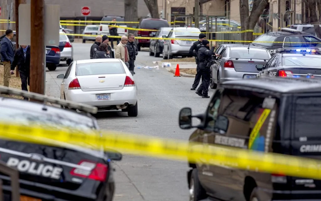 On a quiet street in central Greensboro, flashing blue and red lights illuminate the surrounding area as police officers cordon off the scene of a recent crime. Nearby, investigators meticulously collect evidence—photographing footprints, analyzing bullet casings, and documenting the environment. Residents gather at a distance, their faces a mix of concern and curiosity, as the atmosphere fills with tension and the sounds of police radios. While this neighborhood has seen its share of challenges, the community remains resilient, hopeful for solutions to prevent such tragedies from happening again.